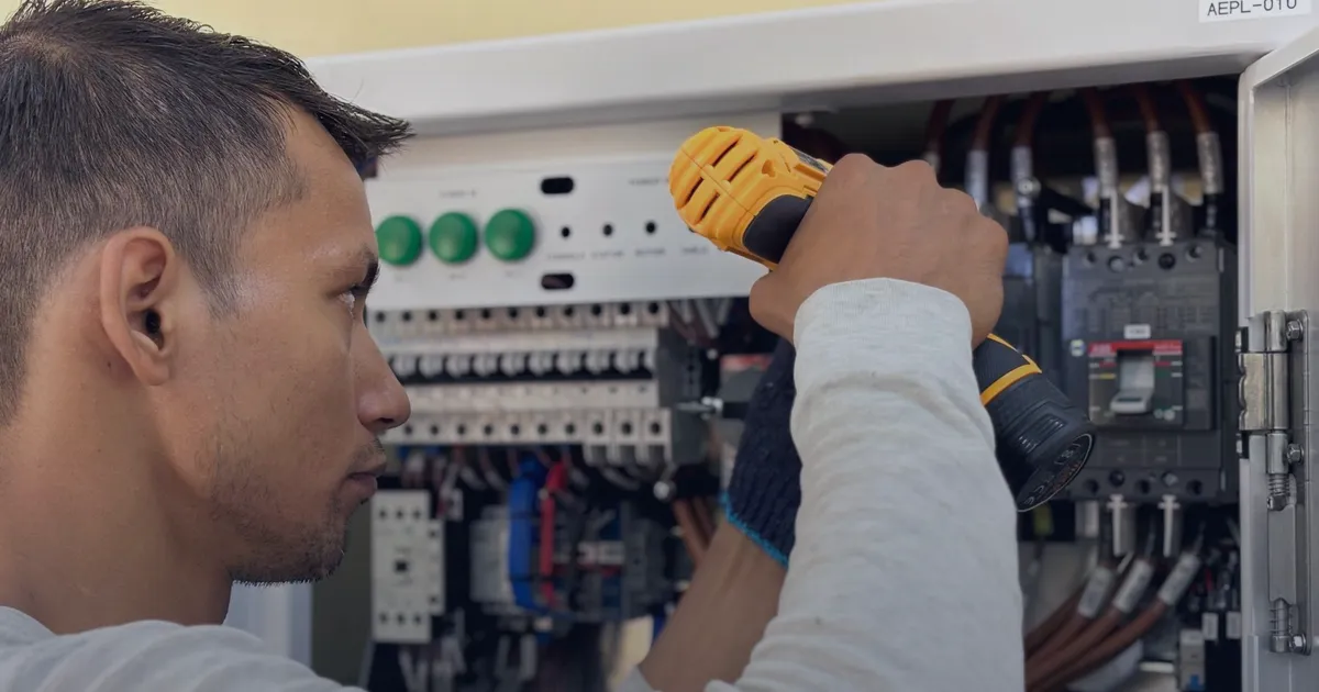 An electrician using a drill on a switchboard