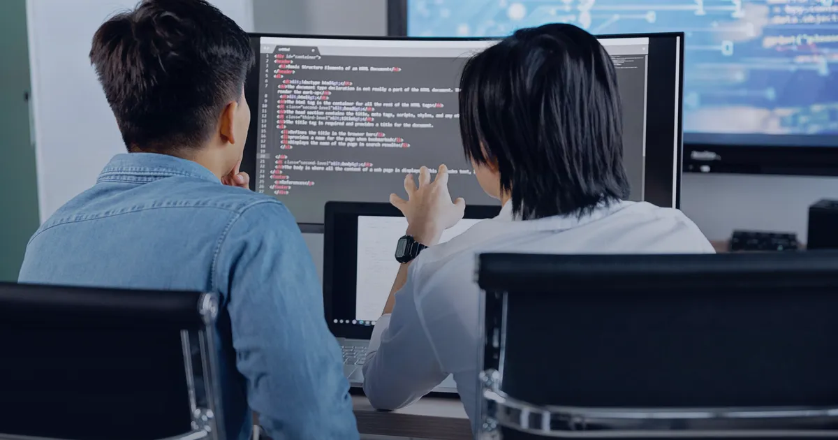 Two developers working side by side at screens full of code