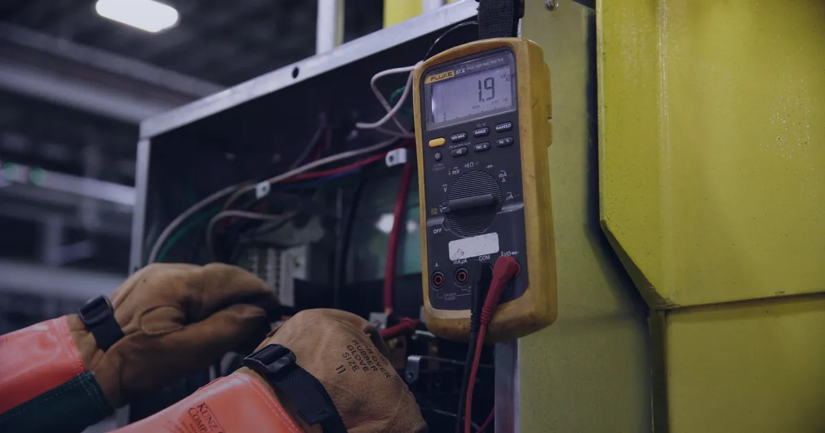 An electrician in safety gloves testing a switchboard with a multimeter