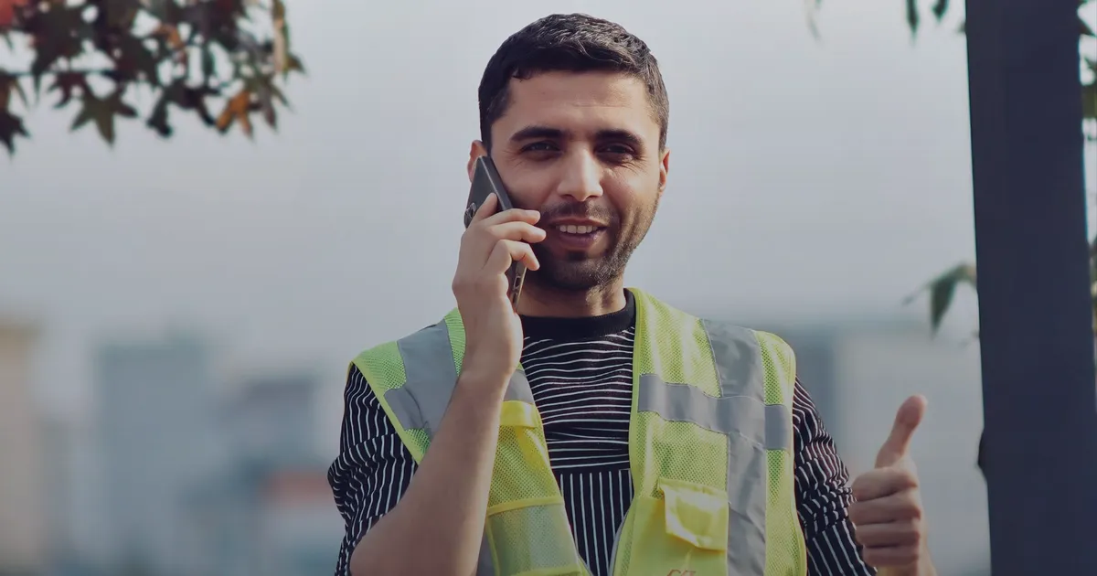 A smiling tradie in a hi-vis vest on the phone, giving a thumbs up